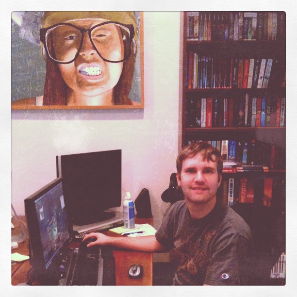 Clay smiling at his desk with a painting of me wearing a viking helmet in the background