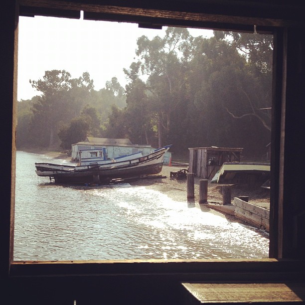 small boat on shore through the window of a wooden structure