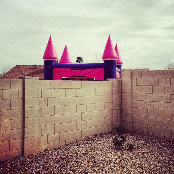 pink and purple bouncy castle on the other side of a concrete block fence