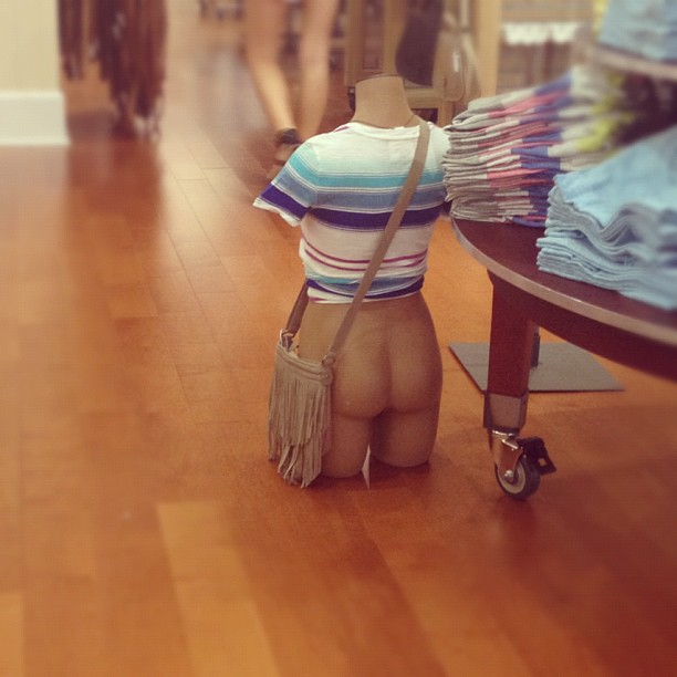 mannequin torso sitting on the floor of a store, it has a shirt on but no pants so its butt is howing