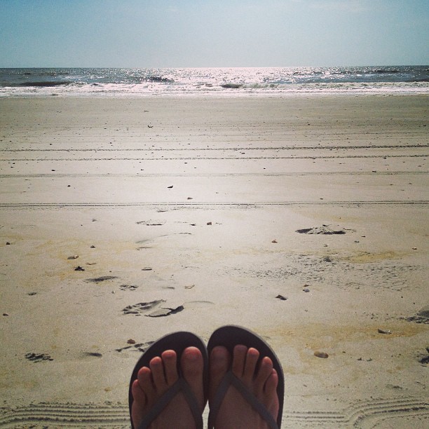 a pair of feet in flip flops on the beach