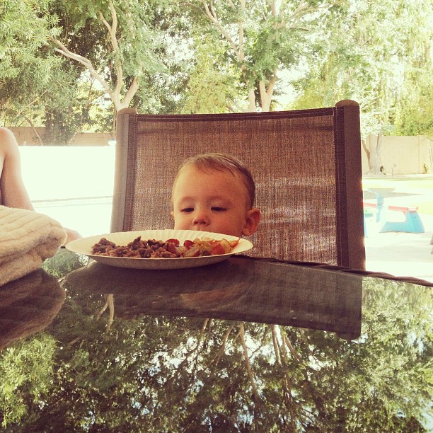 small child’s head barely peeking over a table with a plate of food