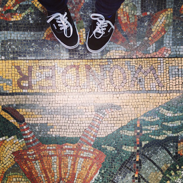 two feet wearing Vans standing on a mosaic tile floor that spells out “Wonder” upside down