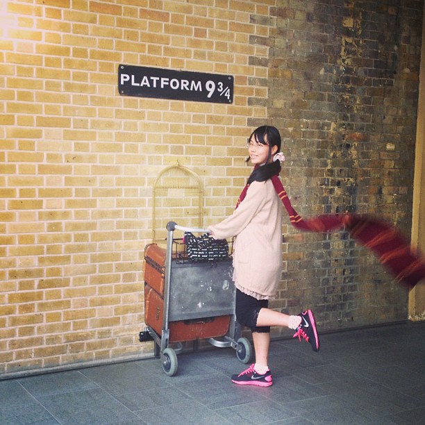 Asian girl posing, pushing a car through the brick wall of Platform 9 and 3/4 