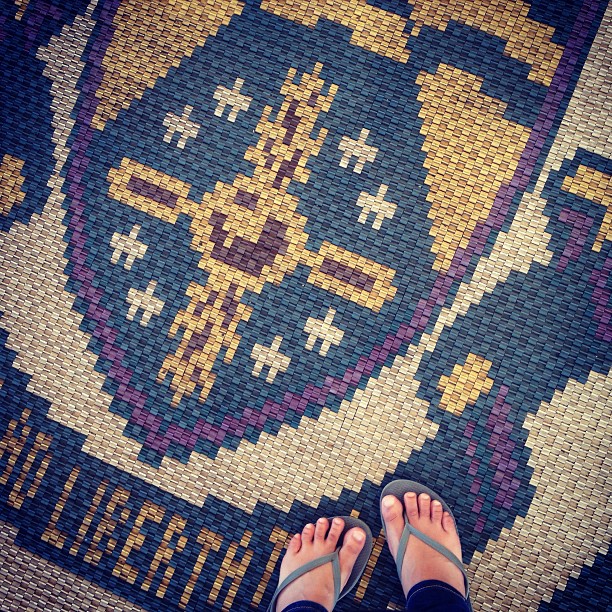 feet in flip flops standing upon a mosaic floor