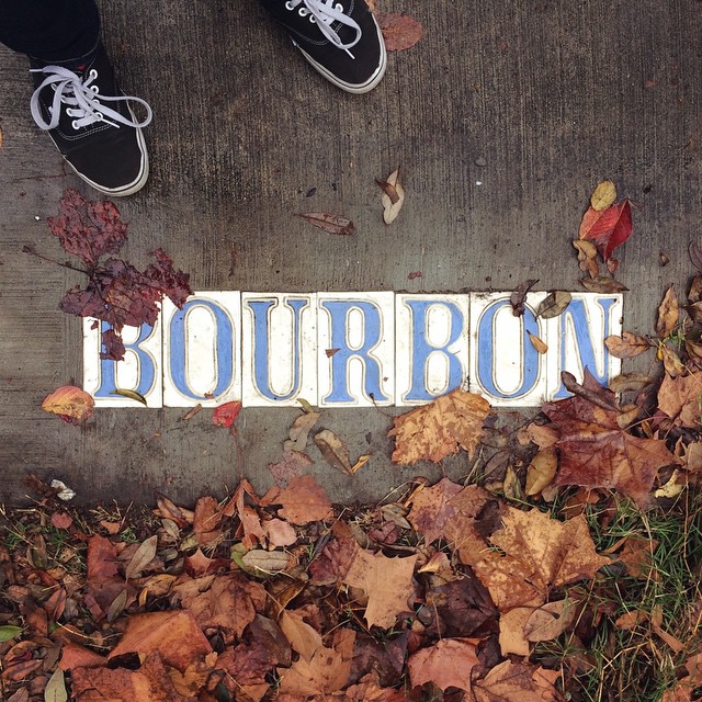 a pair of Vans on the sidewalk over a “Bourbon” sidewalk tile inlay surrounded by grass and fall leaves