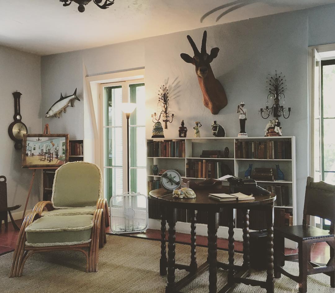 a cozy study with a table and typewriter, bookshelves, and an antelope head mounted on the wall