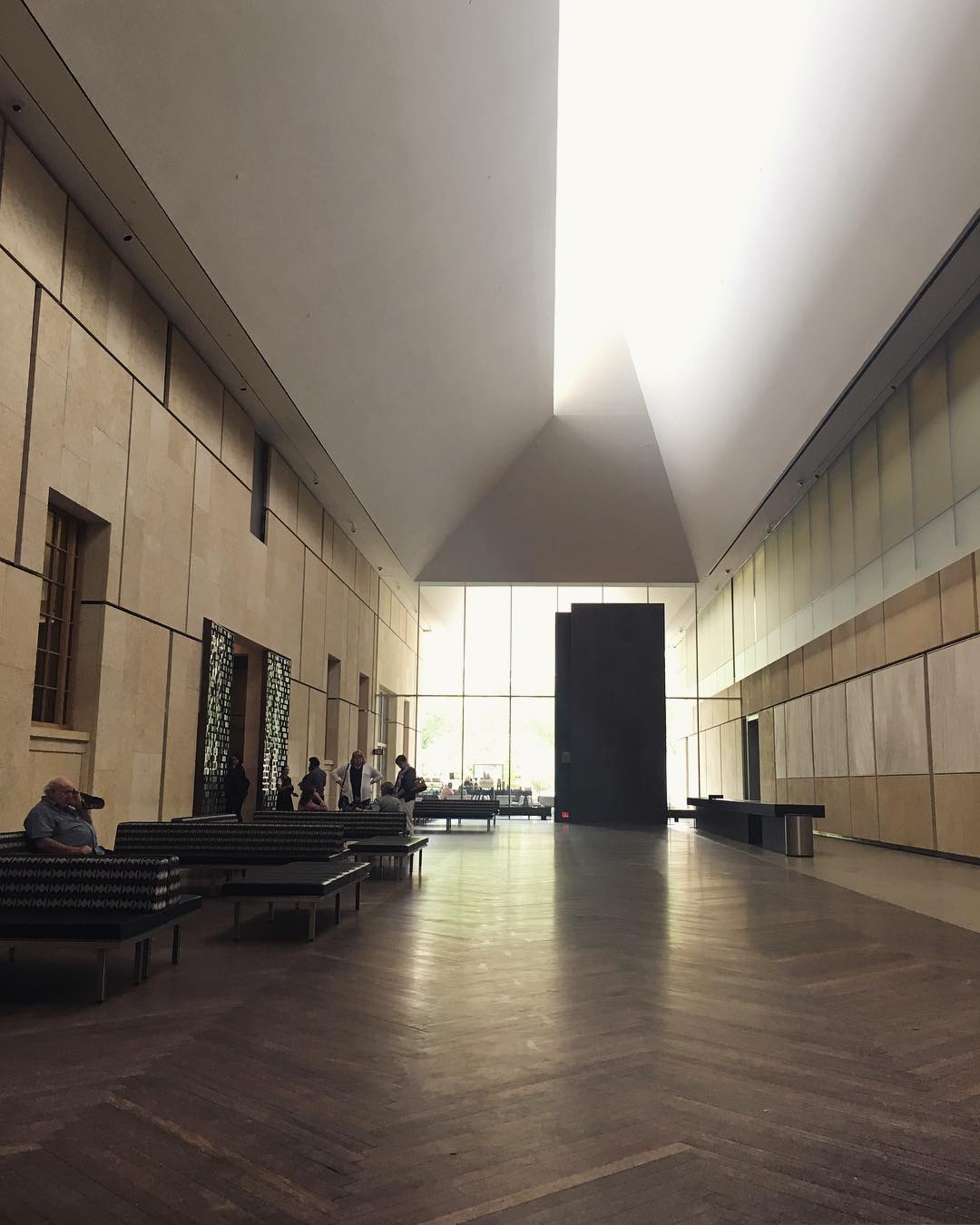 sunlight coming through tall windows at the end of a long corridor with parquet wood floors and high angled ceilings