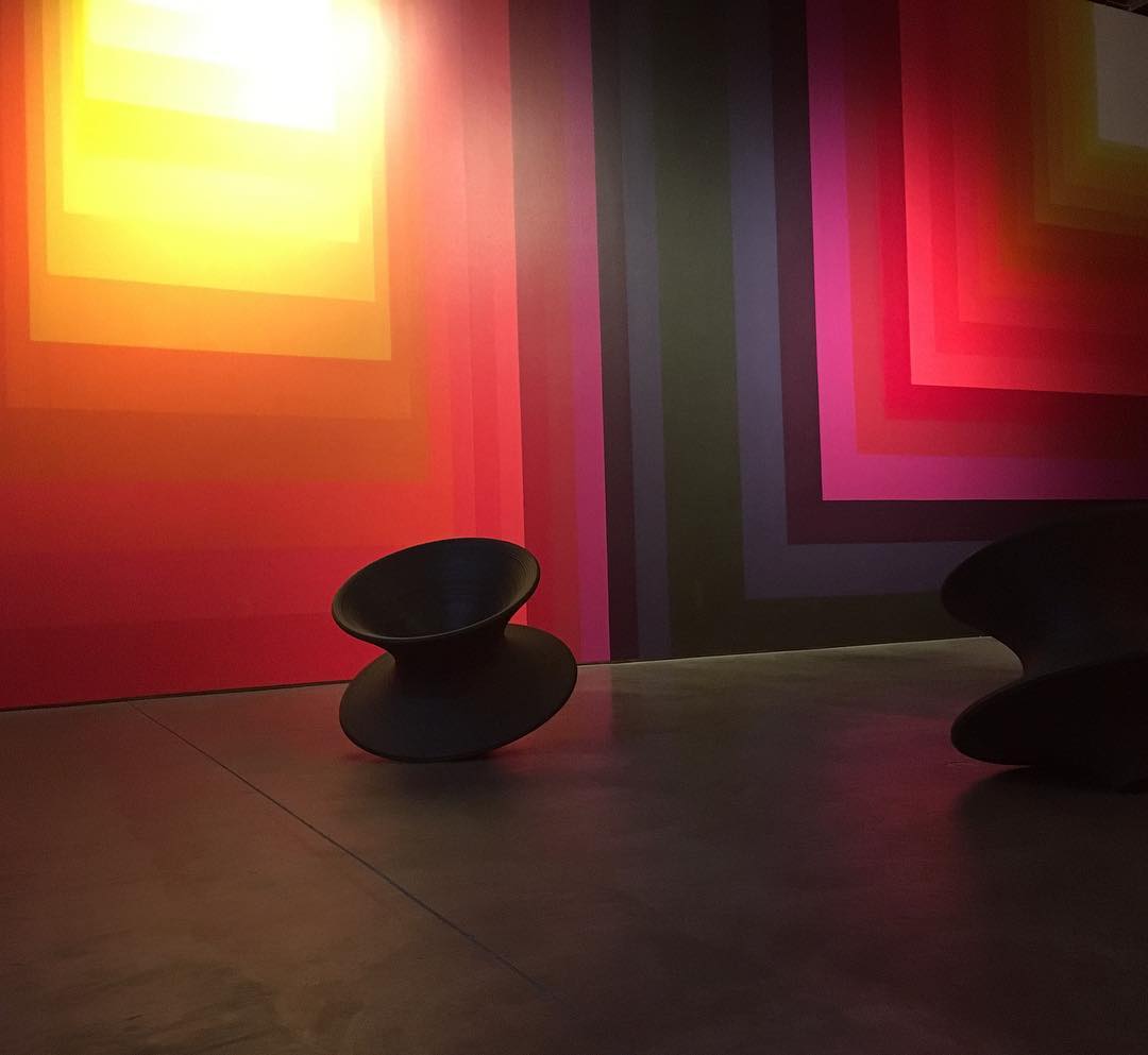 dimly lit room with illuminated walls covered in brightly colored, geometric gradients; black Magis Spun chairs lean on the floor