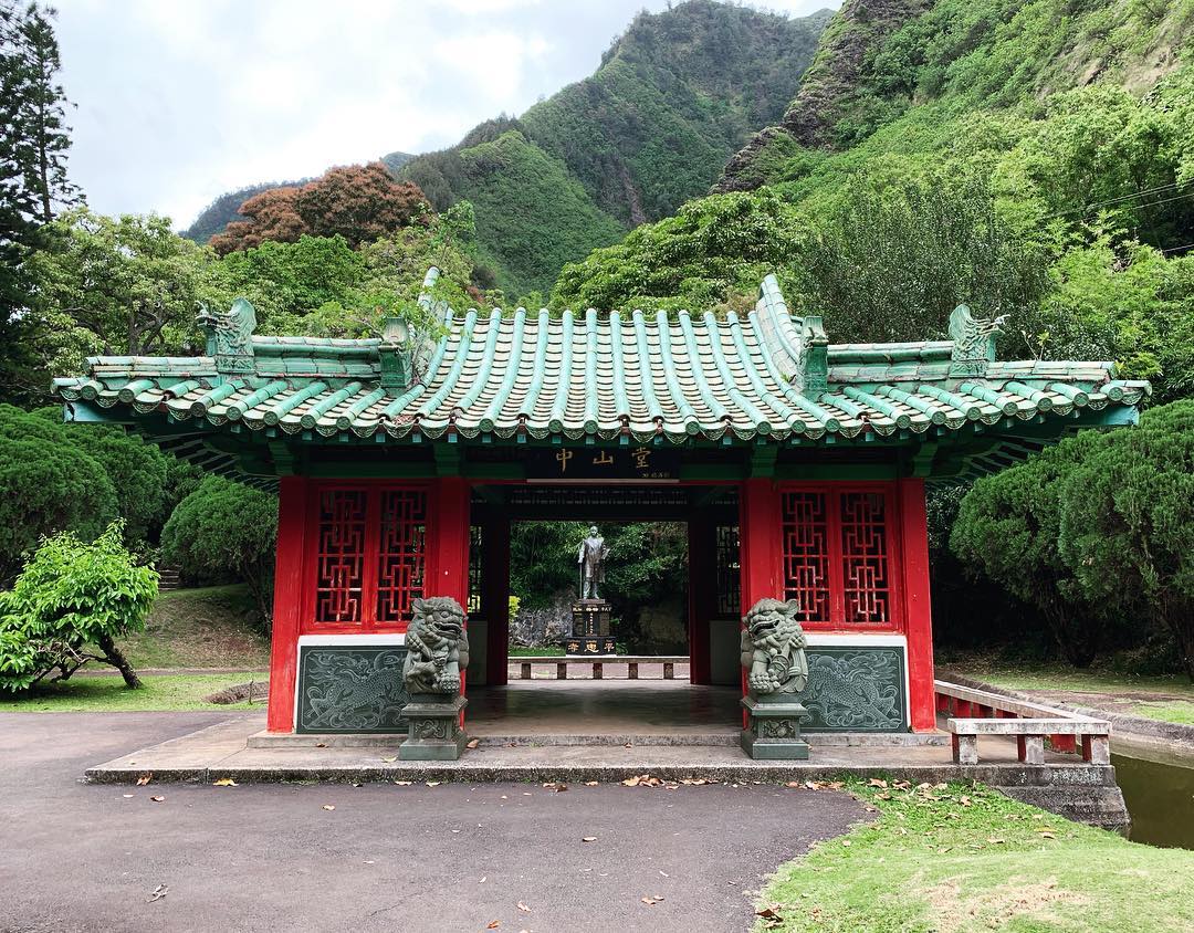 Chinese pagoda with stone foo dogs out front and lush green hills behind