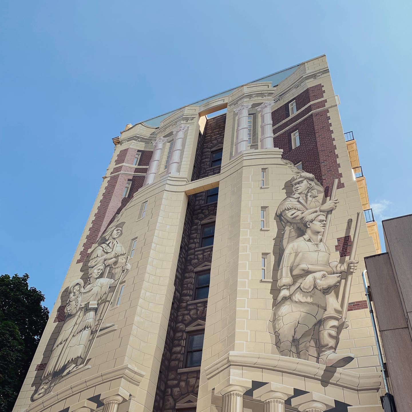 facade of a tall building with a mural of pioneers and Natives