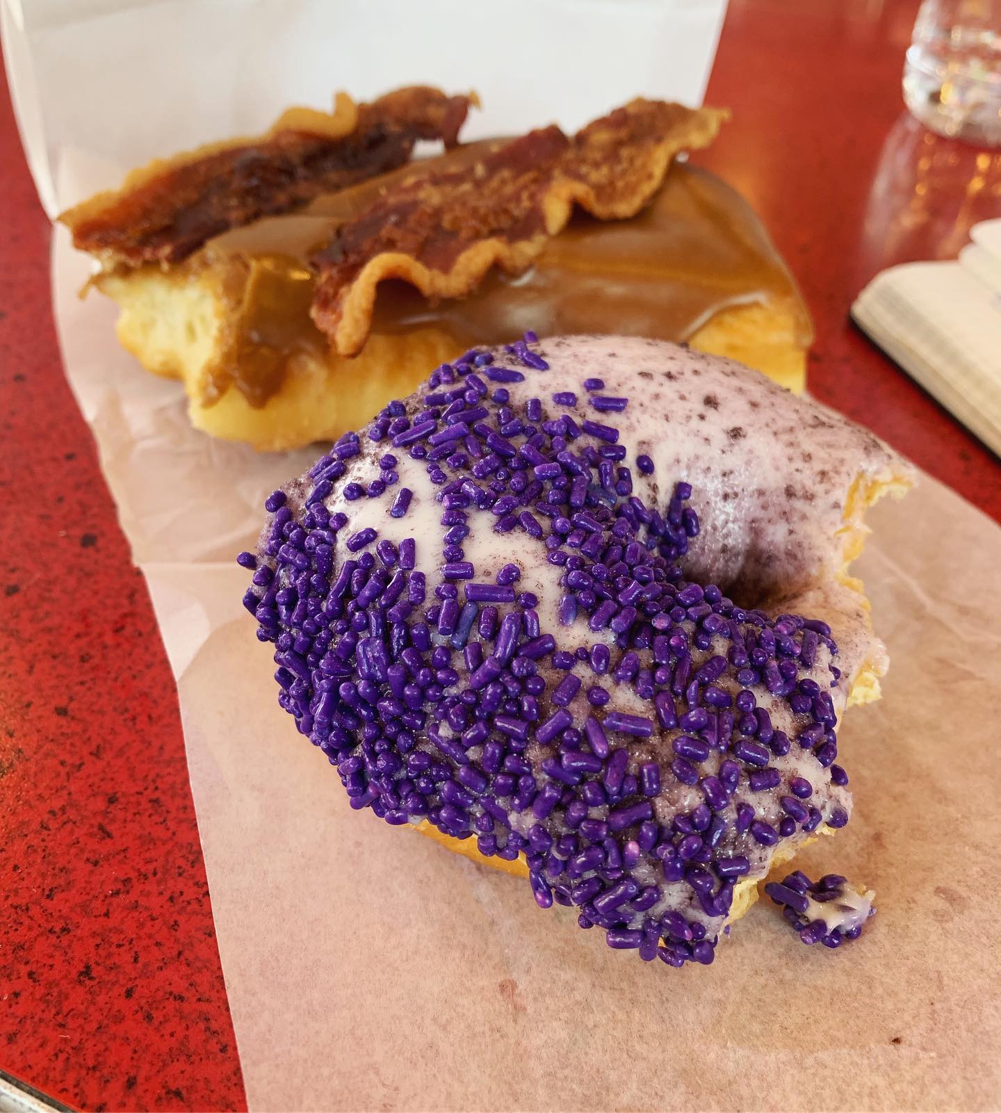 half eaten donuts: a maple bacon bar and a purple donut with sprinkles