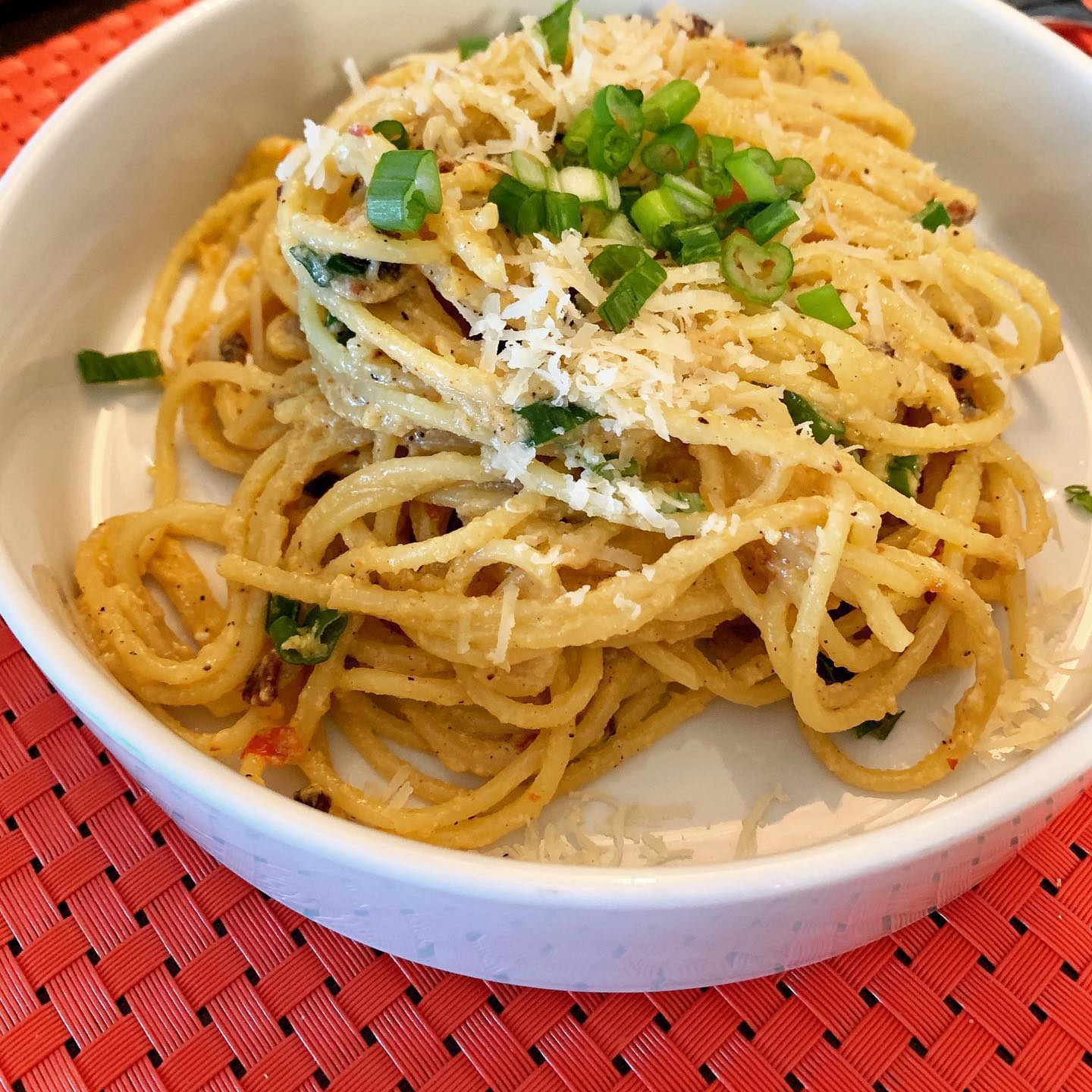 bowl of peppery, creamy spaghetti topped with cheese and scallions