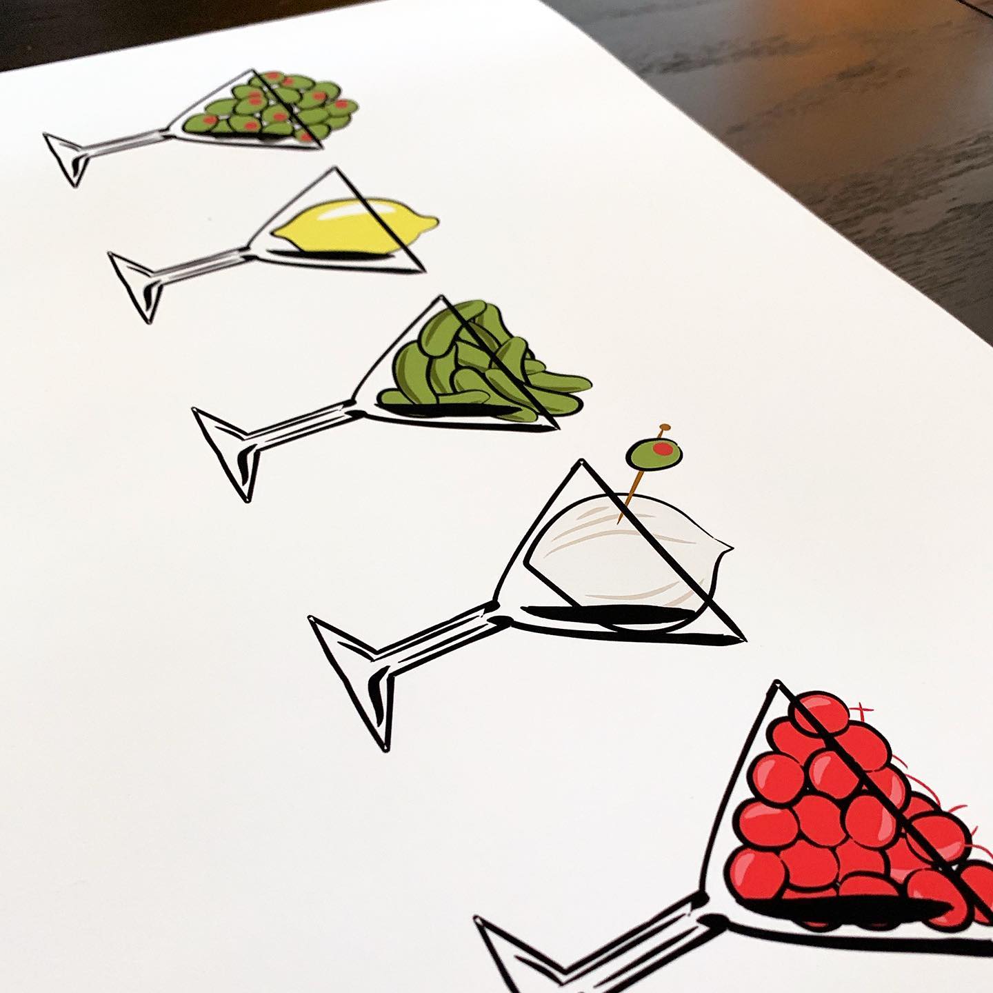 angled photo of printed artwork: five martini glasses filled with olives, a lemon, gherkins, an onion with an olive stuck in it, and cherries