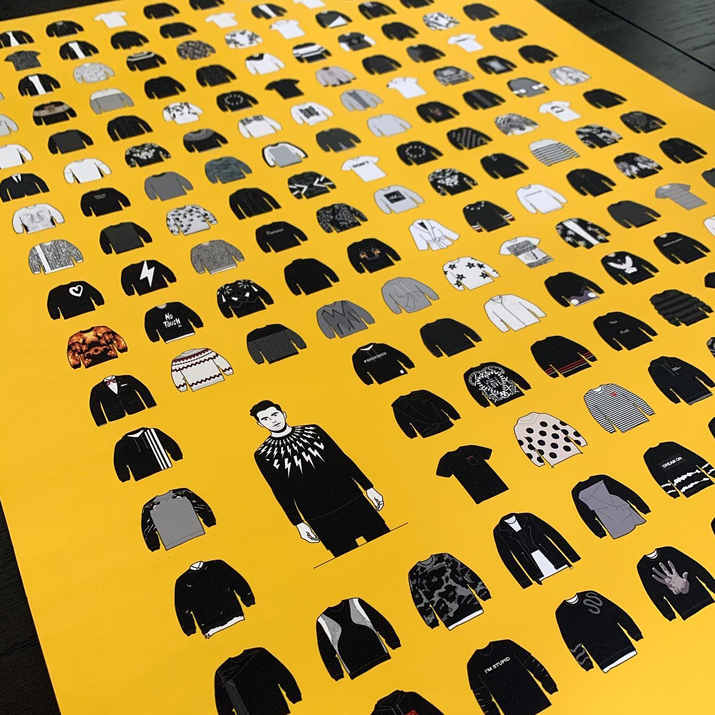 art print featuring a yellow background and grid of black and white shirts and sweaters