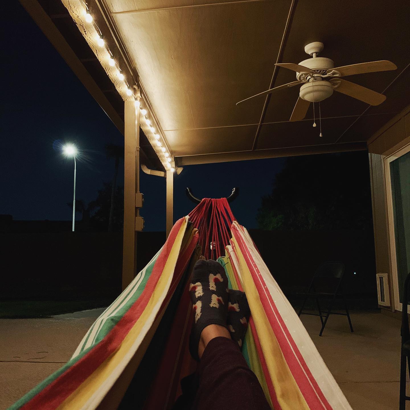 crossed feet in socks inside a colorful hammock on a porch illuminated with string lights